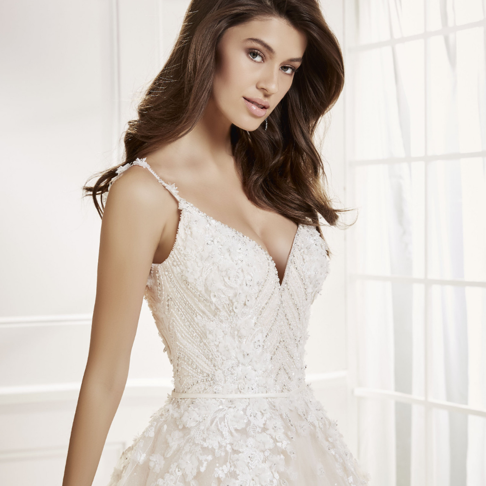 Close up of a brunette model wearing a strappy wedding dress with a beaded floral applique body and v-neckline.
